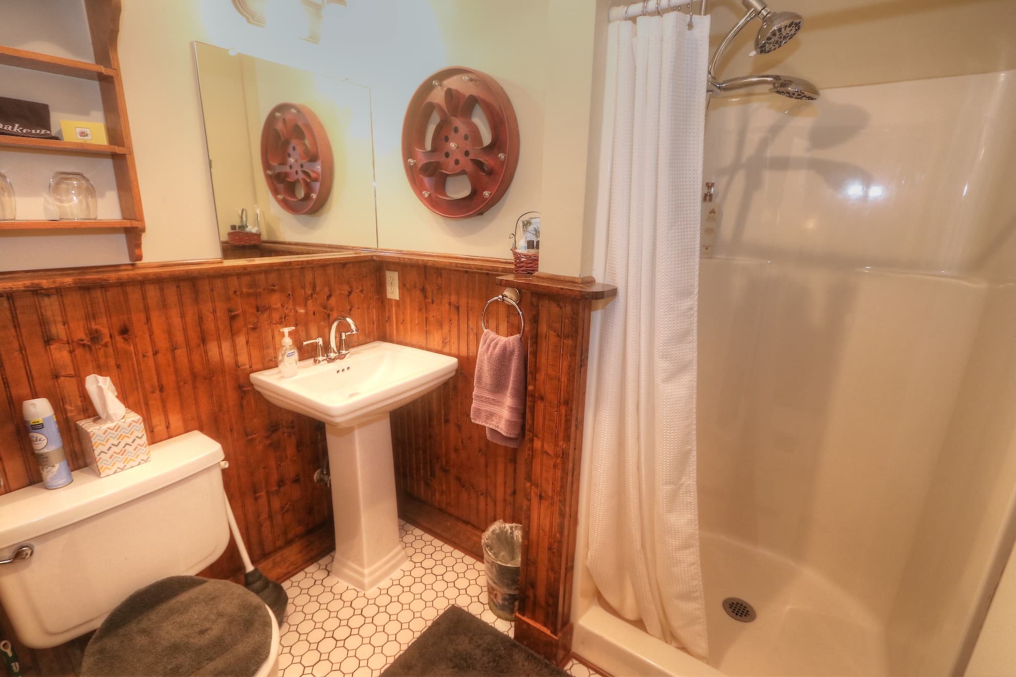 An upstairs bed and breakfast room with brown and floral wall paper, a decorative white metal bed with a red duvet. Also in the room is a brown loveseat and brown ceiling fan