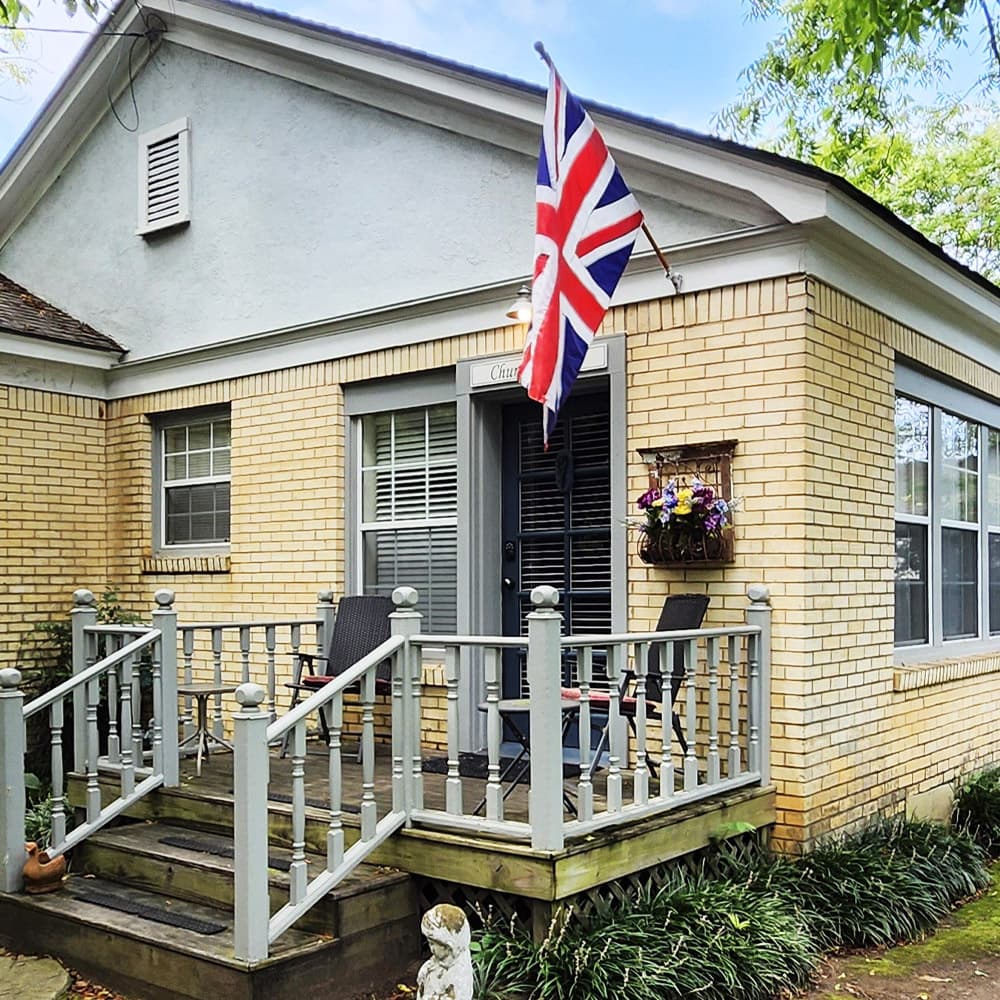 A quaint brick house with a British flag, a small porch, and potted plants.