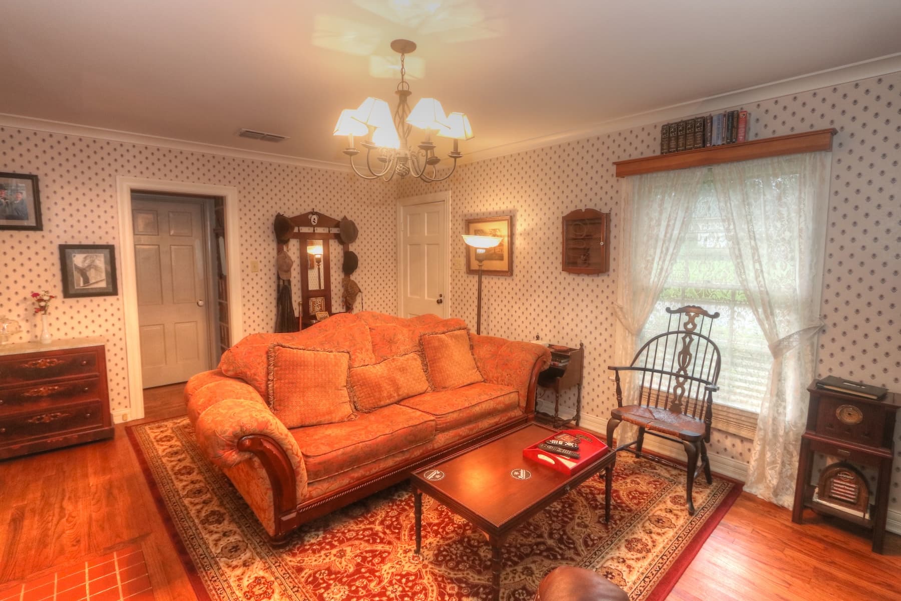 A private bed & breakfast cottage living room with white wallpaper with green dots. Also in the room is a sofa, brown leather recliner, brown coffee table, mock fireplace and wood armoire with tv and dvds