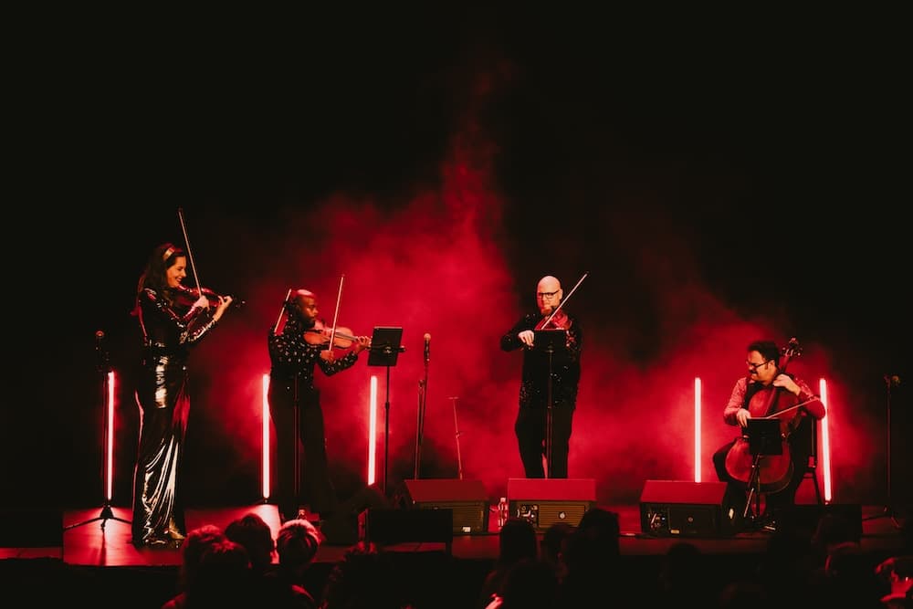 A string quartet performs on stage amidst red lighting and smoke.
