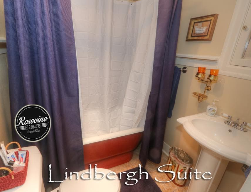 The upstairs Lindbergh Suite Bathroom features a clawfoot tub, blue shower curtain, commode and sink