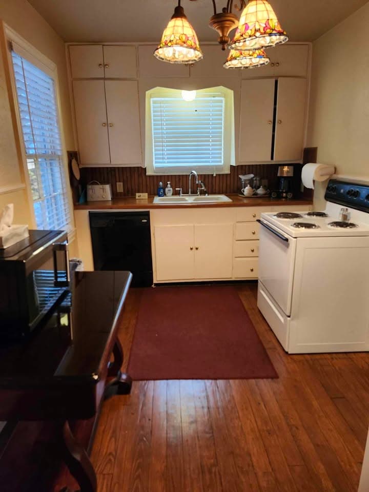 A cozy kitchen featuring white cabinetry, a window above the sink, a wooden countertop, and a rug on the hardwood floor.