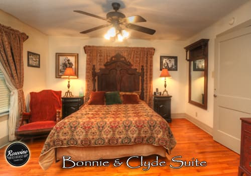 The upstairs Bonnie & Clyde Bedroom features a wood bedframe with duvet, wood floors, brown ceiling fan