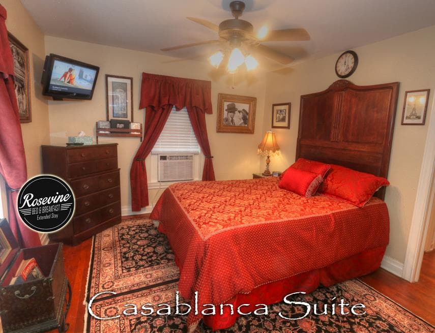 Wooden highback bed is topped with black and gold coverlet. The walls around it feature screen shots from the movie Casablanca and Parisian themed wall art