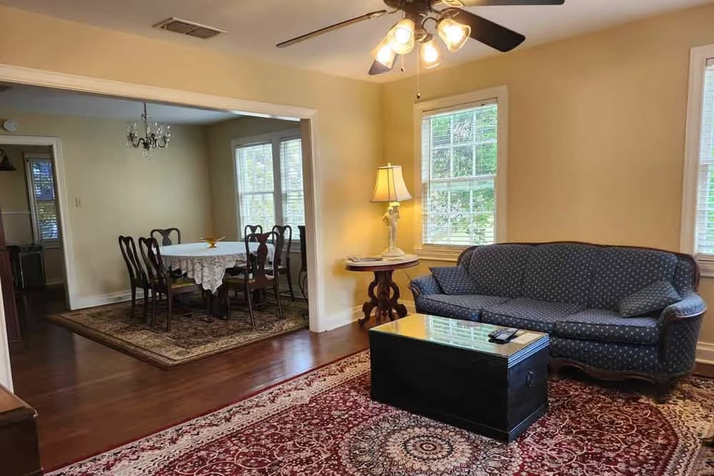 Cozy living room with a blue couch, wooden coffee table, and a view into a dining area featuring a chandelier and a table set for meals.