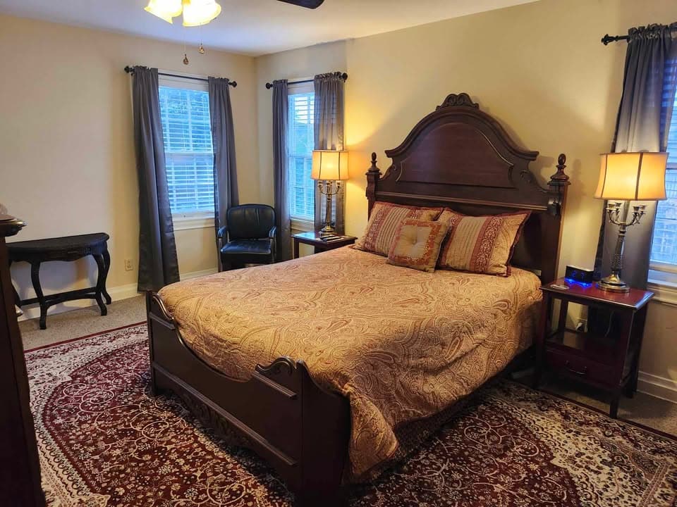 A cozy bedroom featuring a wooden bed, decorative bedding, two lamps, and a window with curtains.