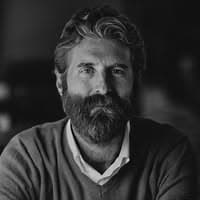 A man with a thick beard and wavy hair gazes directly at the camera.