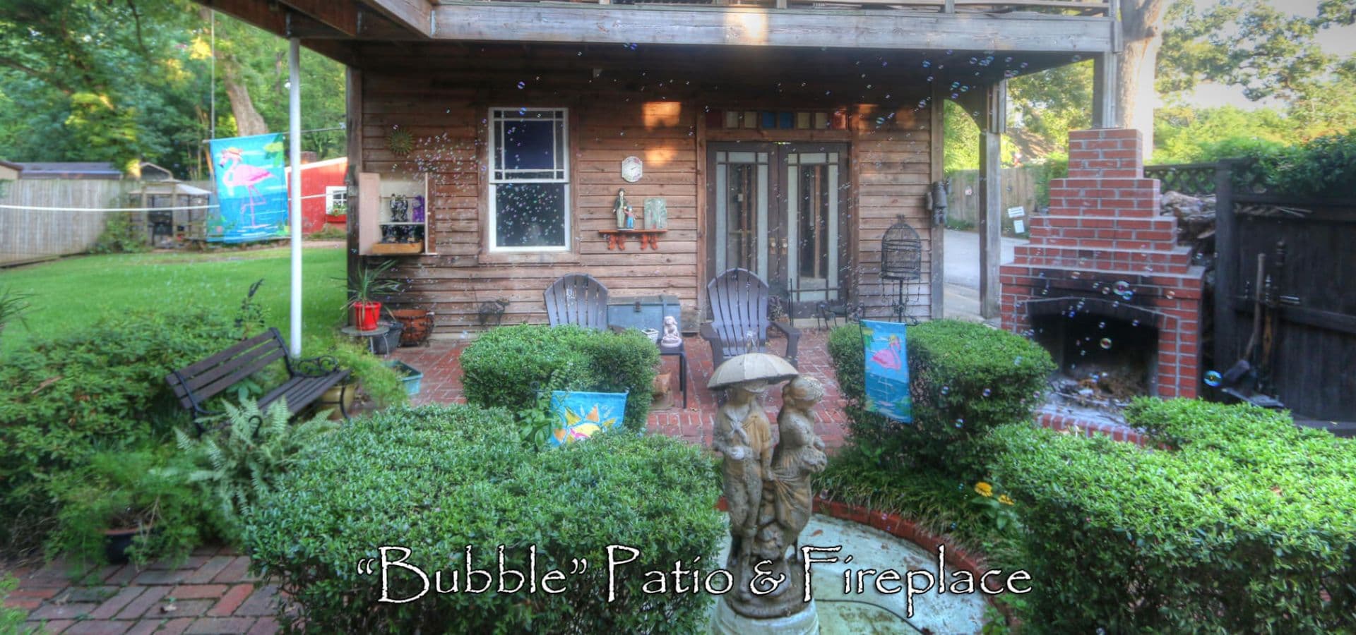 A cozy patio area with a fireplace, surrounded by greenery and decorative elements.