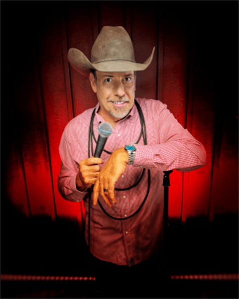 A man in a cowboy hat holds a microphone with a confident smile against a red background.