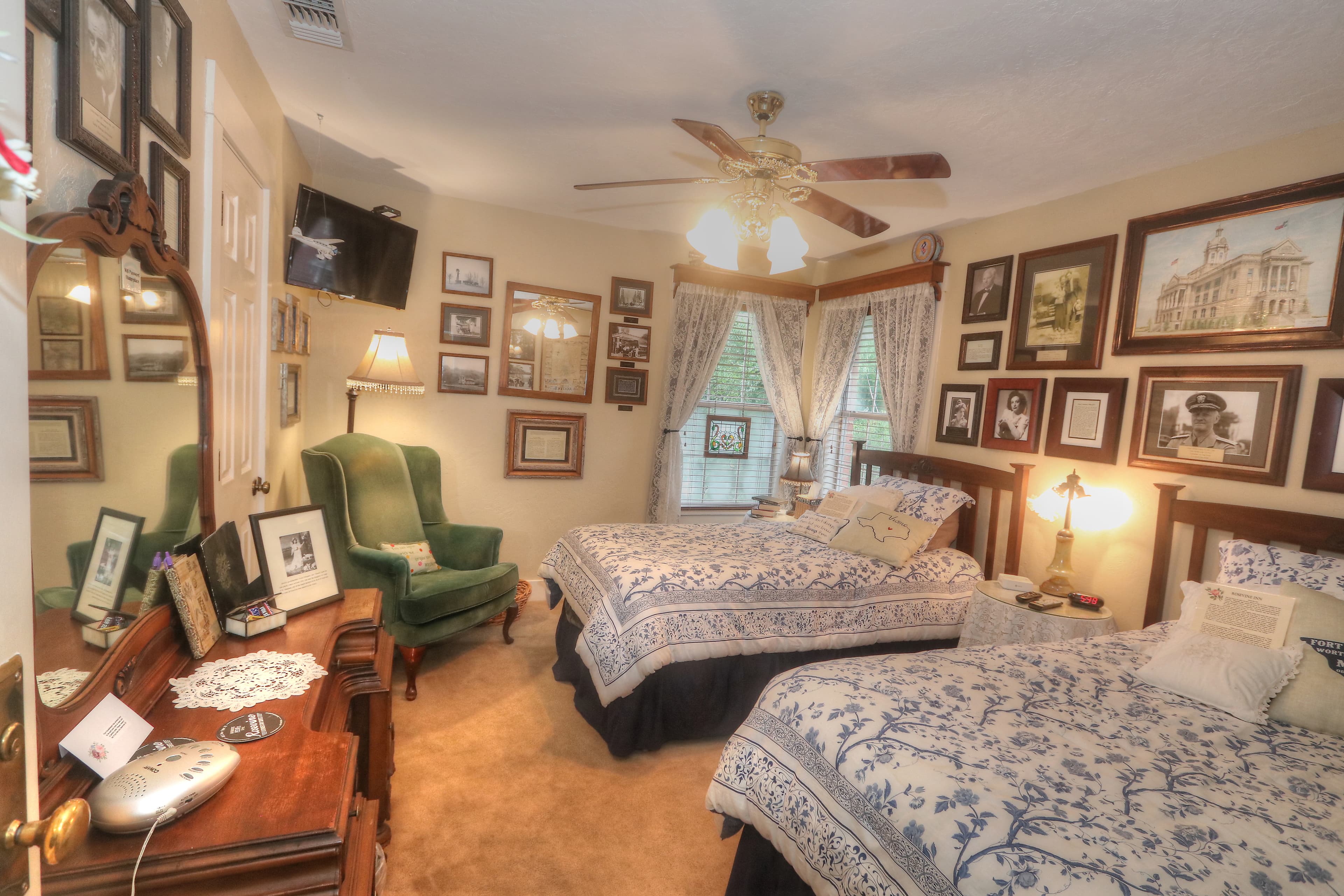 An upstairs bed and breakfast room with two twin beds that have yellow duvets with blue flowers. There is also a dark green highwing back chair and brown ceiling fan