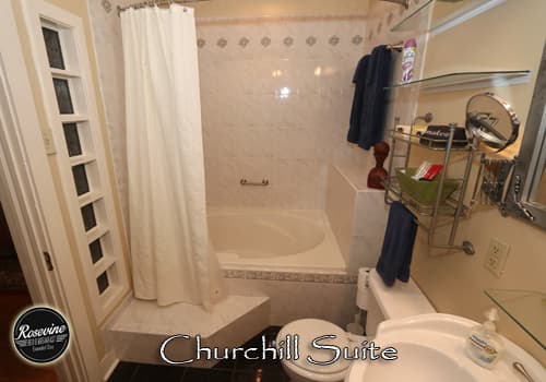 The bathroom in the Churchill Suite with white garden tub and shower combo, commode and sink