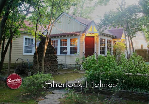The exterior of a private bed & breakfast cottage. Yellow paint, brown wood door and stone fireplace in the courtyard