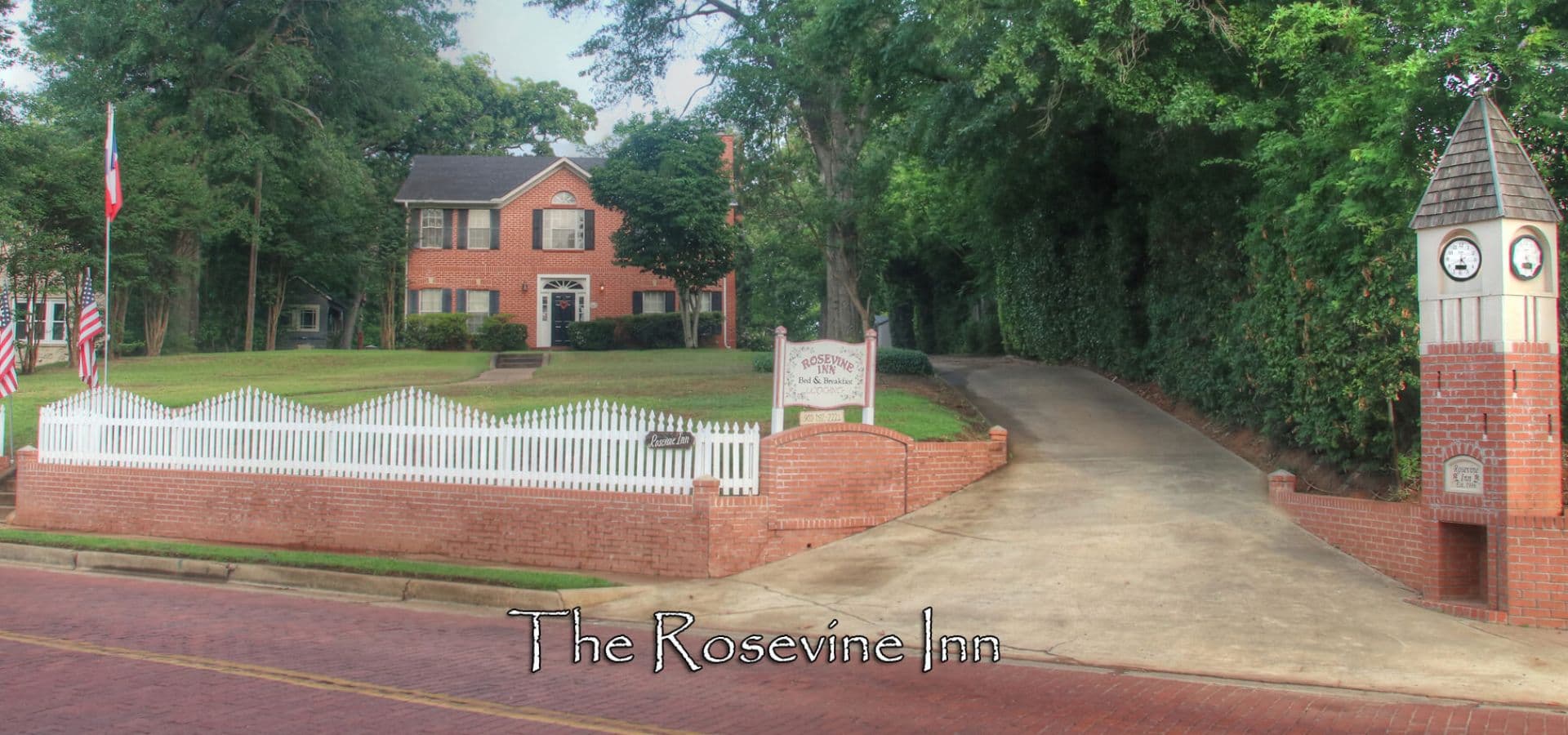 Exterior view of The Rosevine Inn, featuring a brick facade, white picket fence, and a clock tower.