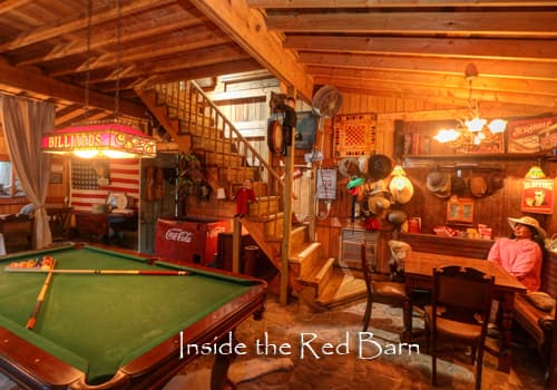 The interior of the barn game room on site has wood walls, a pool table, seating area and wood stairs leading up