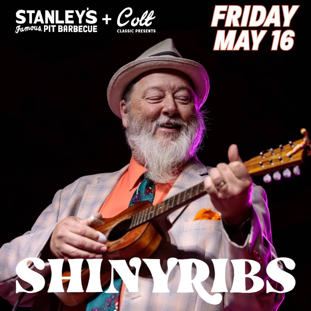 A smiling musician in a colorful outfit plays a small guitar on stage, promoting a BBQ event featuring Shiny Ribs.