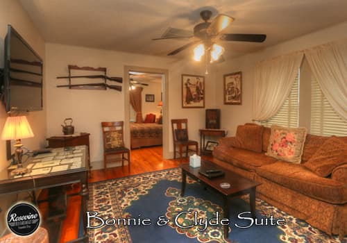 The upstairs Bonnie & Clyde Living Room features wood floors, a brown ceiling fan, brown three seater couch, blue rug and additional chairs for seating