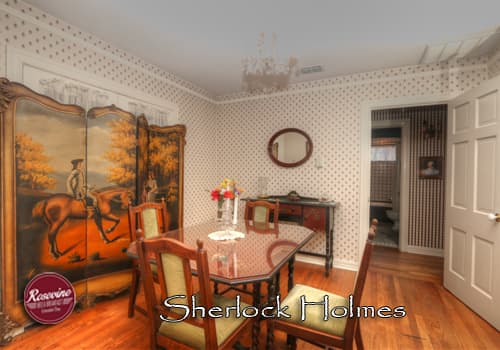 A private bed & breakfast cottage dining room with glasstop table and four wood chairs with green cusions. Also in the room is a brown wood sidee table.