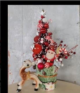 A festive holiday centerpiece with a decorated Christmas tree featuring Santa, red ornaments, and a reindeer figurine.
