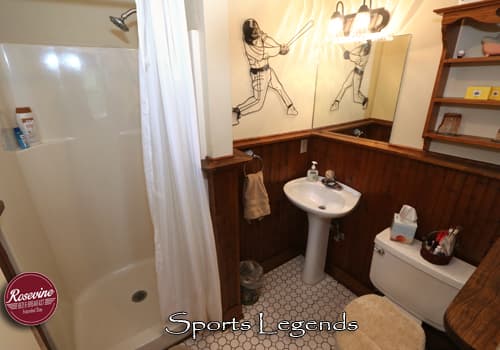 An upstairs bed and breakfast bathroom with creme walls and brown wainscotting. There is a walk in shower, sink and commode.