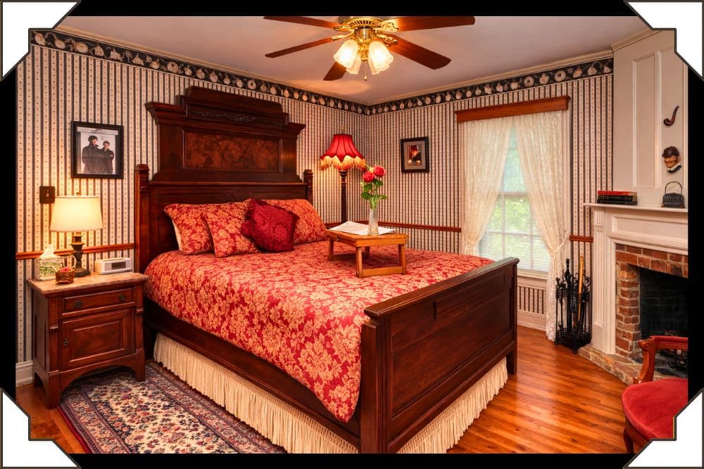 Cozy antique bedroom featuring a floral-patterned bedspread, hardwood floor, and decorative wallpaper.