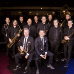 Photo of the group of twelve musicians with their instruments. They all have black on and they are called Beatles to Bourbon