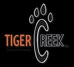 logo-in orange the word Tiger. under that Animal Sactuary next to the word is the sord Creek The C in creek is larger and has 4 images resembling a paw print