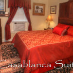 Red and Gold Bedspread with a window unit, tv and brown dresser drawers