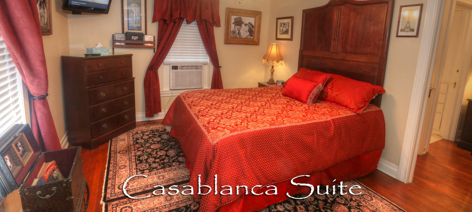 Red and Gold Bedspread with a window unit, tv and brown dresser drawers