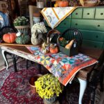 white long sofa table with a quilt on top, green cabinet in the background decorative fall items all around