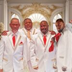 4 men dressed in white suits with red ties with a festive chtistmas gold and white background