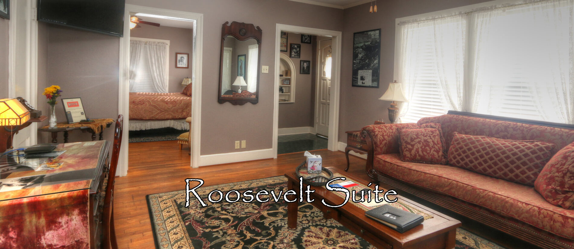 Living room with red and gold sofa, oriental rug and gas fireplace with photograph of Franklin Roosevelt above it