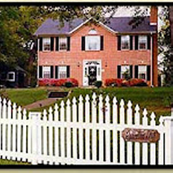 red brick georgian colonial house with grren lawn in front and a whote picket fence in front-sign on right says Rosevine Inn