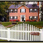 front of red brick house -the Rosevine Inn with a white picket fence in the foreground