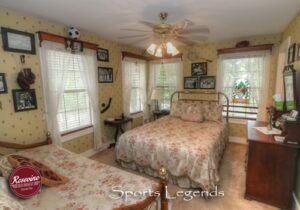 Sports Legend room with floral striped wallpaper, brass Queen bed with white satin spread, and antique dresser with mirror