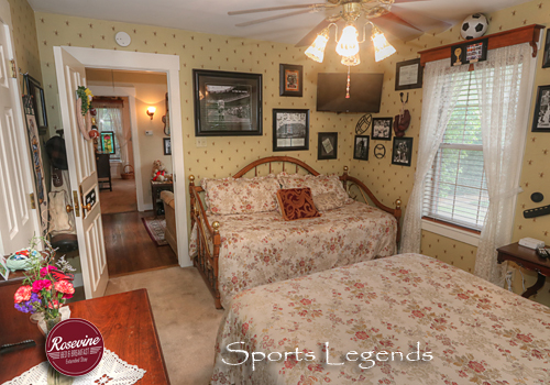 Sports Legend room with floral striped wallpaper, brass Queen bed with white satin spread, and antique dresser with mirror