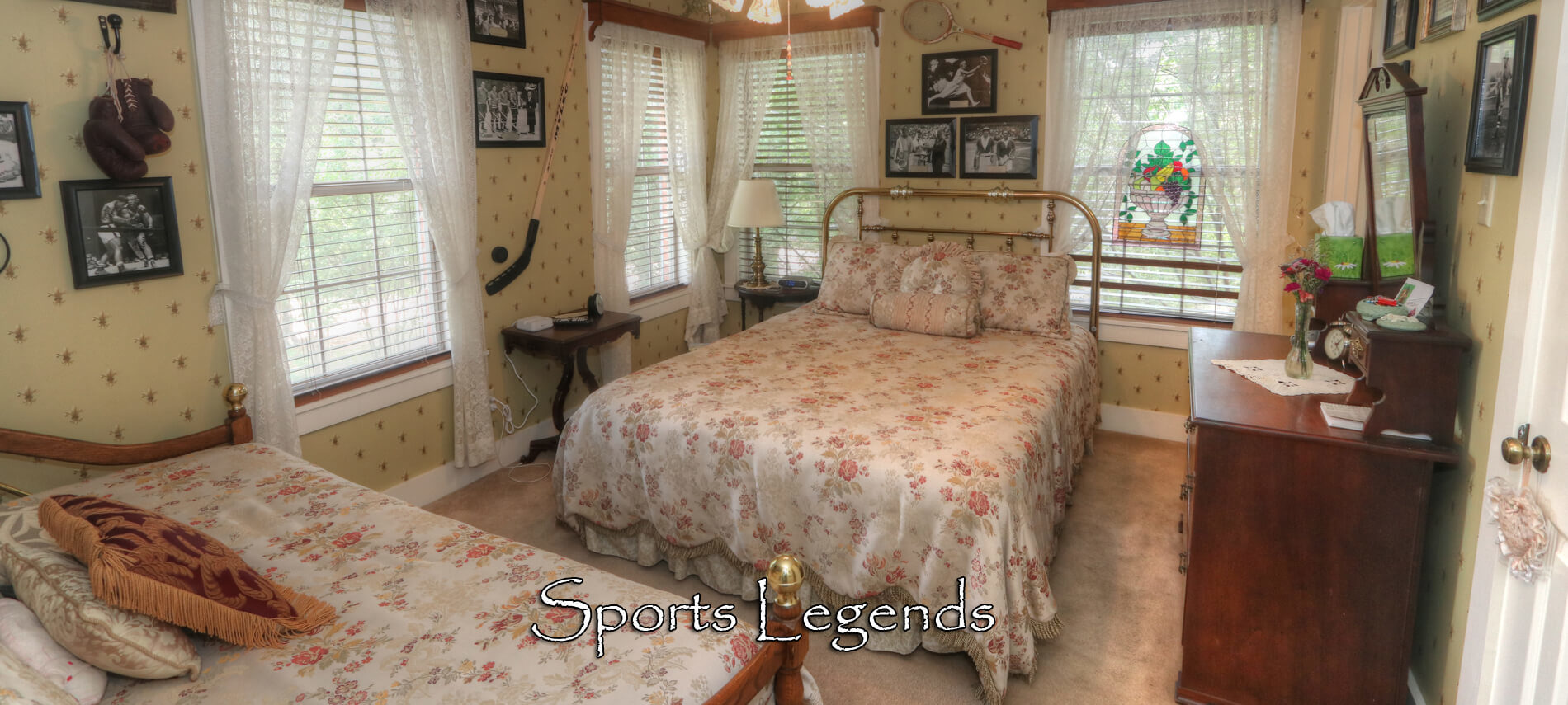 Sports Legend room with floral striped wallpaper, brass Queen bed with white satin spread, and antique dresser with mirror