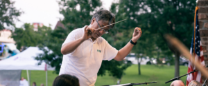 Directorof the East Texas Symphony wearing a pink shirt directing the Symphony at Bergfeld Park. Has a baton in his hand