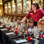 Long table set elegantly with china and wine glasses. Women in a red shirt is pouring red wine.
