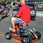 guy in a red shirt and checkered shorts riding a motorized barstool