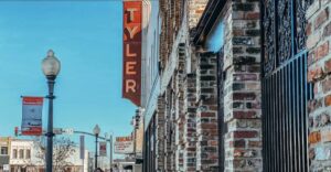 Bright blue sky with some brick buildings in downtown Tyler . Light pole with a banner and The old Tyler Theatre marquee can be seen