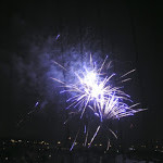 Nighttime sky with a purple and white firework exploding over a lake