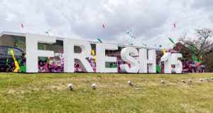 Large white letters on the lawn that say FRESH15 colored balloons in the background