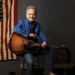 photo of Jimmy Fortune holding a guitar with a blue suit on