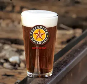 Pint of dark beer with a head on it in a logoed Texas State Railroad glass